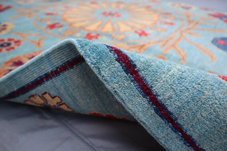 May include: Close-up of a blue rug with a red and cream floral pattern. The rug is folded over, showing the underside with a red stripe.