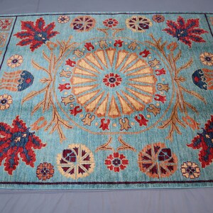 May include: A blue rug with a central medallion featuring a sunburst design. The rug has a border with repeating floral and geometric motifs in red, blue, and gold.
