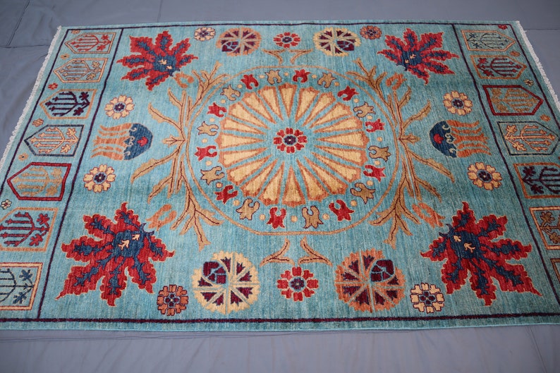 May include: A blue rug with a central medallion featuring a sunburst design. The rug has a border with repeating floral and geometric motifs in red, blue, and gold.