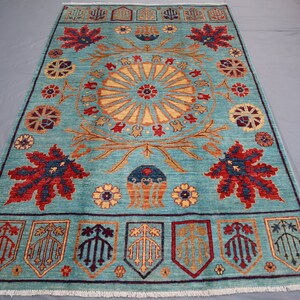 May include: A blue rug with a central medallion featuring a sunburst design. The rug has a border with stylized floral and leaf motifs in shades of red, yellow, and brown.