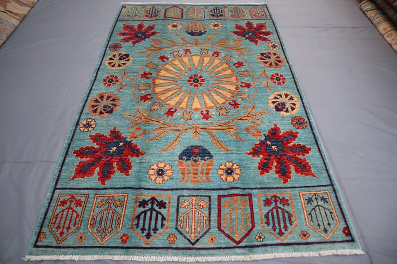 May include: A blue rug with a central medallion featuring a sunburst design. The rug has a border with stylized floral and leaf motifs in shades of red, yellow, and brown.