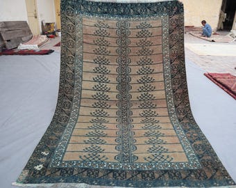 Puede incluir: Una alfombra rectangular con un campo central beige y un borde azul oscuro. La alfombra presenta un patrón repetitivo de motivos estilizados en forma de árbol en azul oscuro. La alfombra se exhibe sobre una superficie gris claro.