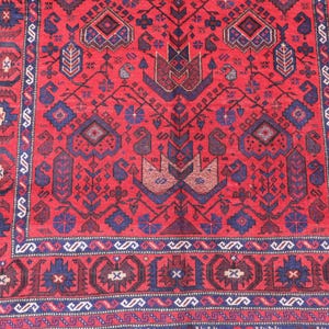 May include: A detailed, red oriental rug with a complex geometric pattern. The rug features a central design with stylized floral and bird motifs in shades of blue and brown, framed by a border with repeating shapes. The rug's intricate design adds a touch of elegance.