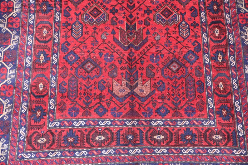 May include: A detailed, red oriental rug with a complex geometric pattern. The rug features a central design with stylized floral and bird motifs in shades of blue and brown, framed by a border with repeating shapes. The rug's intricate design adds a touch of elegance.