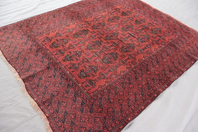 Pode incluir: Um tapete oriental vermelho com um padr&atilde;o geom&eacute;trico detalhado em preto. O tapete apresenta um design central rodeado por uma borda com formas repetidas e franjas nas bordas. O tapete &eacute; provavelmente feito de l&atilde;.