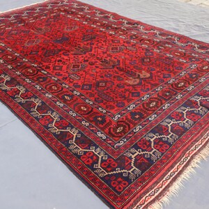 May include: A rectangular, hand-woven rug with a predominantly red field. The rug features intricate geometric patterns in navy blue, beige, and brown, with a detailed border. The rug's edges have a fringe.