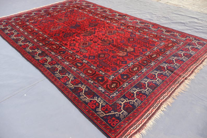 May include: A rectangular, hand-woven rug with a predominantly red field. The rug features intricate geometric patterns in navy blue, beige, and brown, with a detailed border. The rug's edges have a fringe.