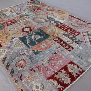 May include: A rectangular patchwork rug with a variety of patterns and colors. The rug features a mix of floral, geometric, and abstract designs in shades of blue, red, pink, and gold. The rug's dimensions are not visible.