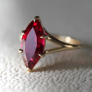 Puede incluir: Un anillo de oro con una gran piedra preciosa de rubí rojo oscuro de forma marquesa.