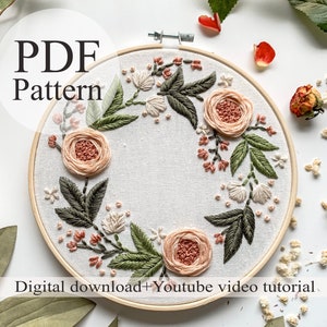 May include: A PDF pattern for a floral embroidery hoop art project. The hoop features a wreath of delicate pink and white flowers with green leaves, stitched on a white fabric background. The text "PDF Pattern" is displayed at the top of the image.