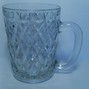May include: A clear glass mug with a diamond pattern. The mug has a handle and is perfect for serving beverages.
