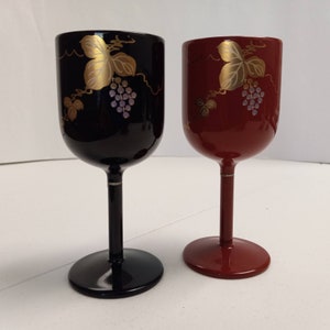 May include: Two small, decorative wine glasses with gold leaf grapevine designs. One glass is black and the other is red.