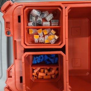 May include: A red plastic toolbox with three compartments. The top compartment contains a variety of small, clear plastic connectors. The middle compartment contains orange and blue wire connectors. The bottom compartment is empty.