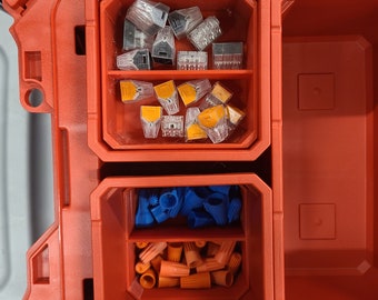Op de afbeelding: Een rode plastic gereedschapskist met drie compartimenten. Het bovenste compartiment bevat een verscheidenheid aan kleine, doorzichtige plastic connectoren. Het middelste compartiment bevat oranje en blauwe draadconnectoren. Het onderste compartiment is leeg.