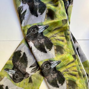 May include: A green silk scarf featuring a repeating pattern of black and white magpies. The birds are depicted realistically with detailed feathers and eyes.