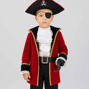 Op de afbeelding: Een kind in een piratenkostuum. Het kostuum omvat een zwart-rode piratenhoed met een doodshoofd en gekruiste botten, een rode jas met gouden randen, een wit gerimpeld overhemd, een zwarte broek, een zwarte riem, een ooglapje en een haakhand.