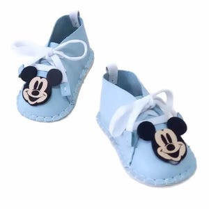 May include: A pair of light blue baby shoes with white laces and a Mickey Mouse character on each shoe.