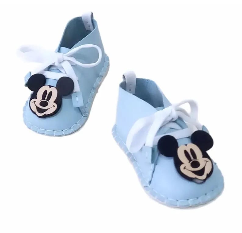 May include: A pair of light blue baby shoes with white laces and a Mickey Mouse character on each shoe.