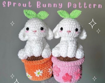 May include: Two white crocheted bunny plushies with green leaves on their heads, sitting in orange and pink crocheted flower pots. The pots have white crocheted flowers on them. The plushies are sitting on a hand.