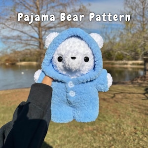 May include: A handmade white bear wearing a light blue pajama suit with a hood and button closure. The bear has black eyes and a small black nose. The text "Pajama Bear Pattern" is at the top of the image.