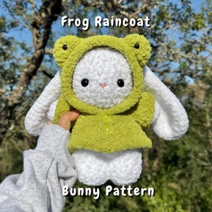 May include: A handmade white bunny plushie wearing a green frog raincoat. The plushie has black eyes and a pink nose. The raincoat has a hood with black eyes and a button closure. The text "Frog Raincoat" and "Bunny Pattern" are visible.