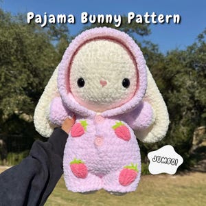 Op de afbeelding: Een pluche konijn met crèmekleurige vacht in een lichtroze pyjama met capuchon, aardbeienpatroon, twee roze knopen en lange oren. De tekst Pajama Bunny Pattern staat bovenaan en het woord JUMBO! staat in een witte wolk.