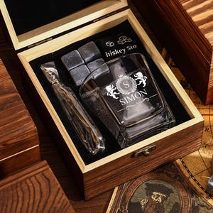 May include: A wooden gift box set containing a rocks glass with "SIMON" printed on it, whiskey stones, and a stainless steel ice wand. The box is open, revealing the contents on a black velvet lining.