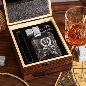 May include: A wooden gift box set with a whiskey glass, ice cubes, and tongs. The glass is engraved with a monogram and the name "MICHAEL". A second glass with initials "JS" is also visible. The set includes whiskey stones.