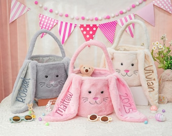 May include: Three plush bunny-shaped Easter baskets with personalized names and the year 2023 embroidered on the ears. The baskets are gray, pink, and white.