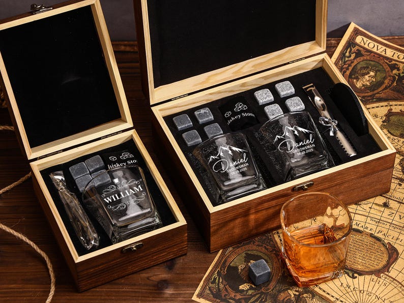 May include: Two wooden gift boxes with whiskey glasses, ice stones, and a metal tool. One box has a glass with "William" etched on it. The other box has two glasses with "Daniel" etched on them. A glass of amber liquid sits nearby.