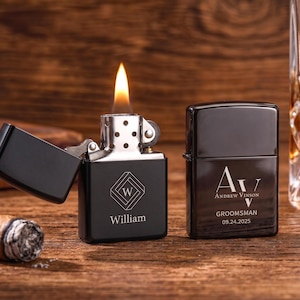Könnte beinhalten: Zwei schwarze Feuerzeuge, eines mit Flamme, und eine brennende Zigarre auf einer Holzoberfläche. Das offene Feuerzeug trägt den Namen "William" und ein geometrisches Design. Das geschlossene Feuerzeug trägt den Namen "Andrew Vinson" und das Datum "09.24.2025".