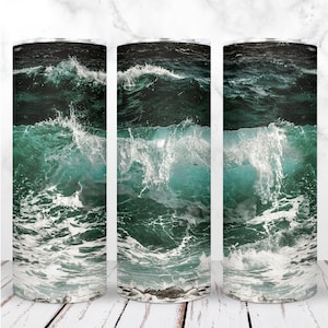 May include: Three stainless steel tumblers with a design of ocean waves crashing on a beach. The waves are a dark green and blue color with white foam.