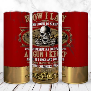 May include: A red tumbler with a gold base and rim, featuring a skull with guns and the text "NOW I LAY ME DOWN TO SLEEP...A GUN I KEEP...WILL BE YOUR LAST RIDE". The design includes bullet casings.