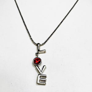 Colar com letra "O" em tom prateado "LOVE" e strass vermelho assinado por Cookie Lee