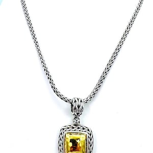 Pode incluir: Colar prateado com um pendente quadrado com uma pedra central dourada. O pendente é emoldurado por uma borda prateada texturizada. A corrente tem um design tecido.