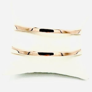 May include: Two rose gold bands, likely rings, are displayed on a white surface. The bands have a smooth, reflective surface, and the light catches them, creating highlights and shadows. The bands are simple and elegant.