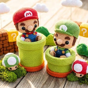 May include: Crocheted figures of Mario and Luigi in green pipes, with a red and green mushroom, green grass, and a brick wall. The figures are wearing their signature hats and overalls. White clouds hang above the figures.