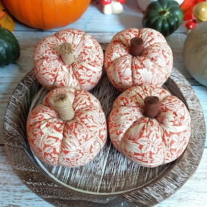 May include: Four fabric pumpkins with cream and orange floral patterns sit on a wooden tray. Each pumpkin has a brown stem. The pumpkins are a festive autumn decoration.