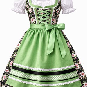Op de afbeelding: Een traditionele Duitse dirndl jurk. De zwarte lijfje heeft een bloemenpatroon en groene rand, gecombineerd met een witte blouse. De groene schort heeft zwarte en witte linten en kant. Een groene strik siert de taille.