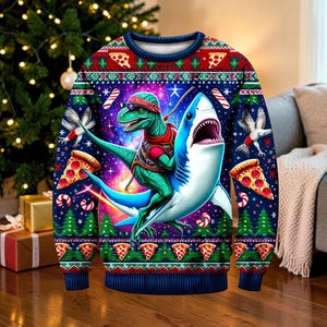 May include: A long-sleeved crew-neck jumper featuring a vibrant graphic print of a green dinosaur wearing sunglasses and a red bandana riding a blue shark. The background displays a cosmic space scene with pizza slices, candy canes, and pine trees.