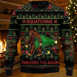 May include: A black long-sleeve crewneck jumper featuring a repeating green and red geometric pattern. The central graphic depicts a brown Bigfoot carrying a green Christmas tree wrapped in colourful light bulbs, with the text SQUATCHING THROUGH THE SNOW.