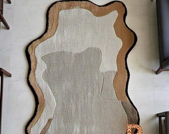 May include: A beige, brown, and white abstract area rug with a black border. The rug has an irregular, organic shape.
