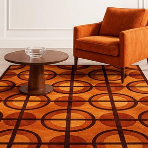May include: An orange retro-style area rug with a geometric pattern of circles and squares. A matching orange armchair and a dark brown round coffee table with a glass bowl are in the room. The rug is a focal point.