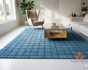 Può includere: Un tappeto rettangolare di un blu vivace con un motivo a griglia blu scuro. Il tappeto presenta una superficie testurizzata e trapuntata con un design quadrato ripetitivo. Nell'angolo in basso a destra, un logo riporta MAISON RUGSA HANDCRAFTED TEXTILES.