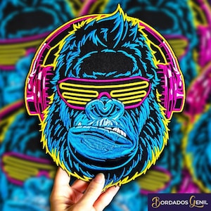 Puede incluir: Un parche bordado de un gorila azul y negro con gafas de sol amarillas fluorescentes y auriculares rosas. El gorila tiene una expresión seria y mira hacia adelante.