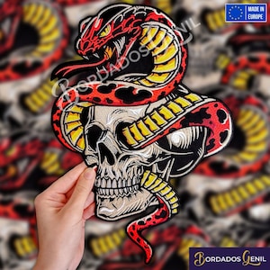 Peut inclure: Un patch brodé noir et blanc représentant un crâne avec un serpent rouge et jaune enroulé autour. La tête du serpent est ouverte et ses crocs sont visibles. Le patch est fabriqué en Europe.