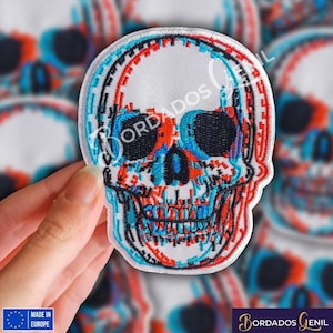 Könnte beinhalten: Ein weißer gestickter Patch mit einem 3D-Schädel-Design. Der Schädel ist schwarz umrandet und mit roten, blauen und weißen Pixelmustern gefüllt. Der Patch ist in Europa hergestellt.