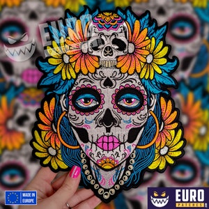 Op de afbeelding: Geborduurde strijkpatch met een kleurrijke Día de Muertos suiker schedel met bloemen en een schedel erop. De schedel heeft roze en blauwe make-up, en de bloemen zijn geel, oranje en blauw.