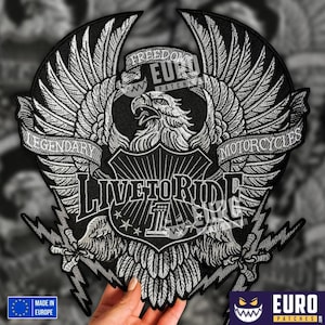 Könnte beinhalten: Ein schwarz-weißer, gestickter Aufnäher mit einem Adlerdesign, die Flügel weit ausgebreitet. Der Text enthält "LIVE TO RIDE", "LEGENDARY MOTORCYCLES" und "FREEDOM EURO PATCHES". Blitze und Sterne akzentuieren das Design. Der Aufnäher wird von einer Hand gehalten.