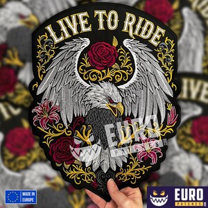 Peut inclure: Écusson brodé avec un aigle aux ailes déployées, des roses et le texte "LIVE TO RIDE" en blanc. Le design comprend des accents dorés et rouges sur fond noir. Fabriqué en Europe.
